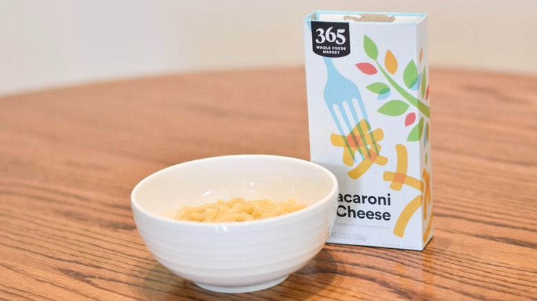 A box of 365 macaroni and cheese next to a white bowl of prepared macaroni