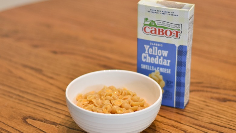 A bowl of macaroni and cheese next to a Cabot box