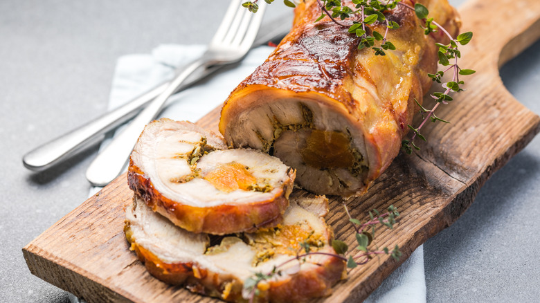 A roll of porchetta sliced on a wooden cutting board