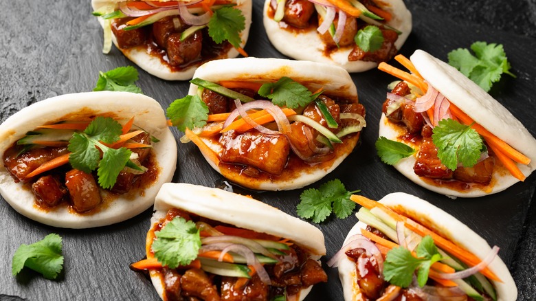 Pork belly pieces inside bao buns with sauce and vegetables