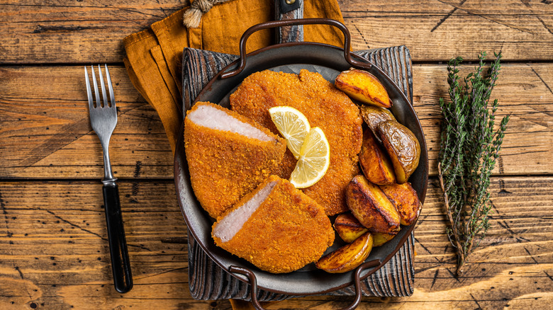 plated pork schnitzel on wooden table with fabric napkins and herbs