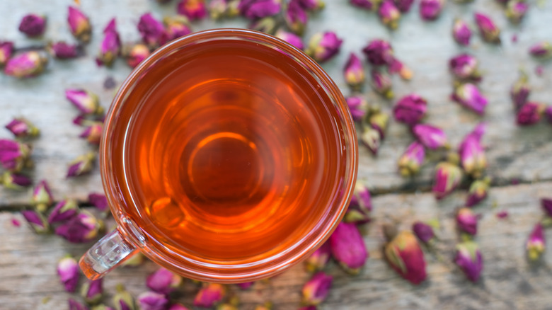 clear cup of tea surrounded by rose petals