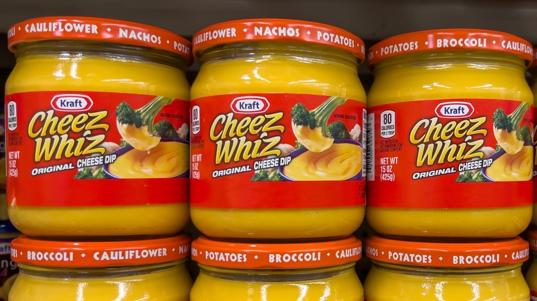 Three glass jars of Cheez Whiz on a store shelf.