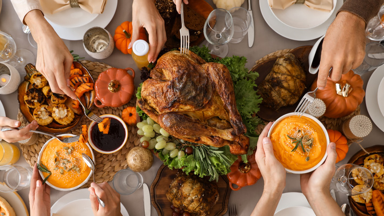 People serving Thanksgiving foods at a full table