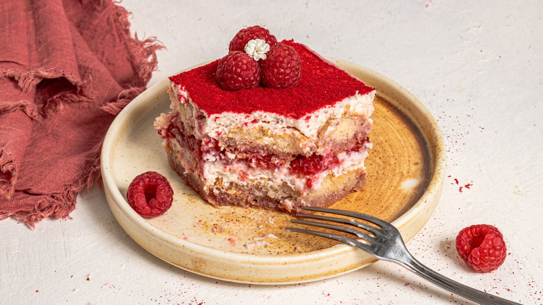 Slice of raspberry and cream tiramisu on a plate and a fork on the side