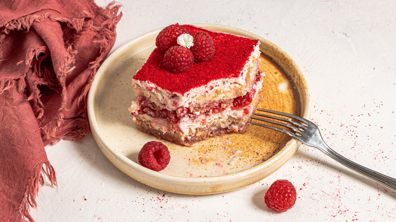 Slice of raspberry and cream tiramisu on a plate with a red napkin on the side