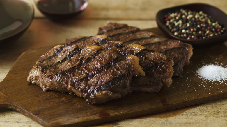 Steak on a cutting board with salt and peppercorns