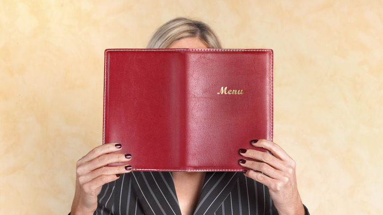 Woman holding bound menu in front of her face