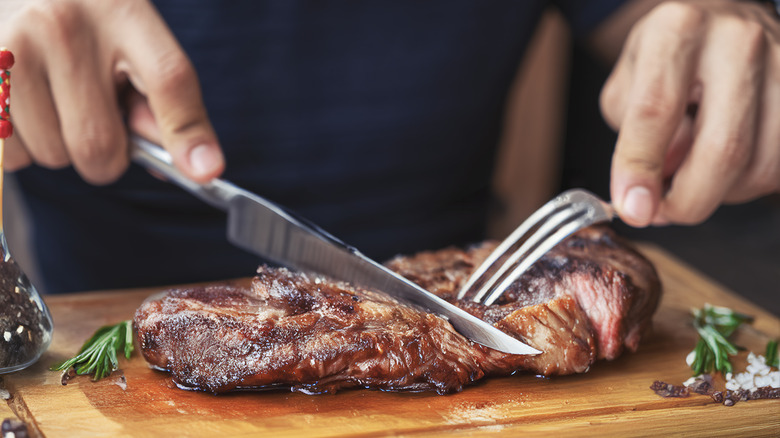 Hands cutting a steak on a cutting board