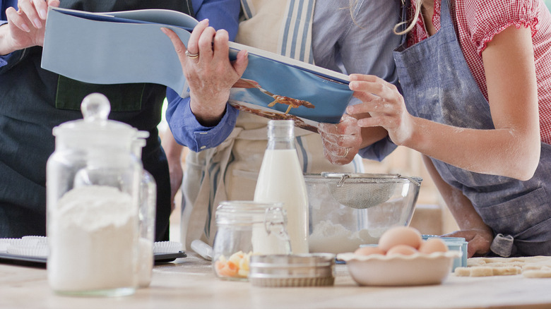 People huddled around a cookbook and baking ingredients