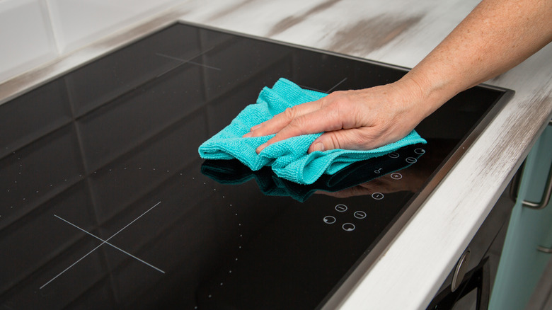 Someone wiping a glass stovetop with a microfiber cloth