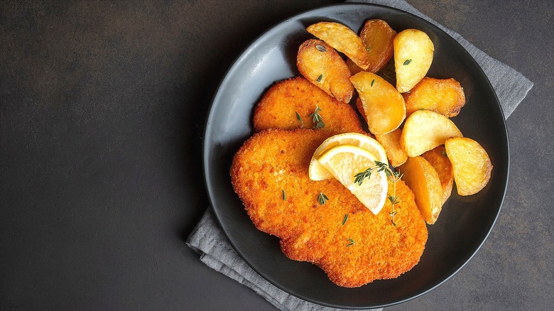 Chicken Milanese with roasted potatoes on a black plate