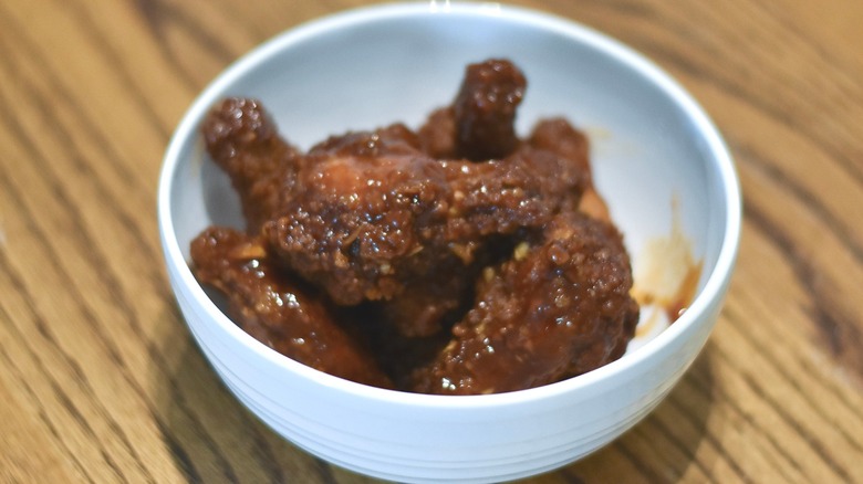 A white bowl of chicken wings with sauce on a wooden table