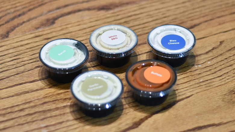 A collection of labeled sauces in black containers on a wooden table