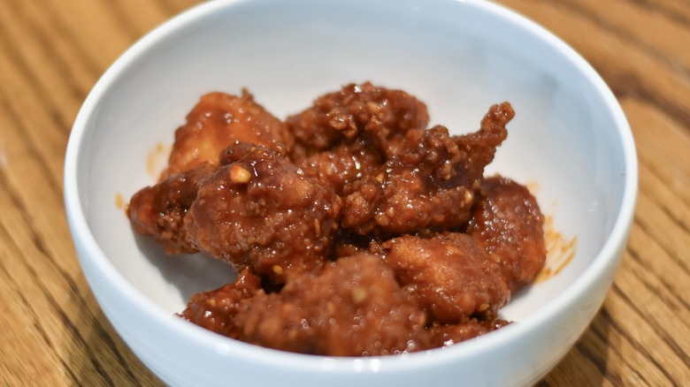 A white bowl of boneless chicken wings with sauce on a wooden table