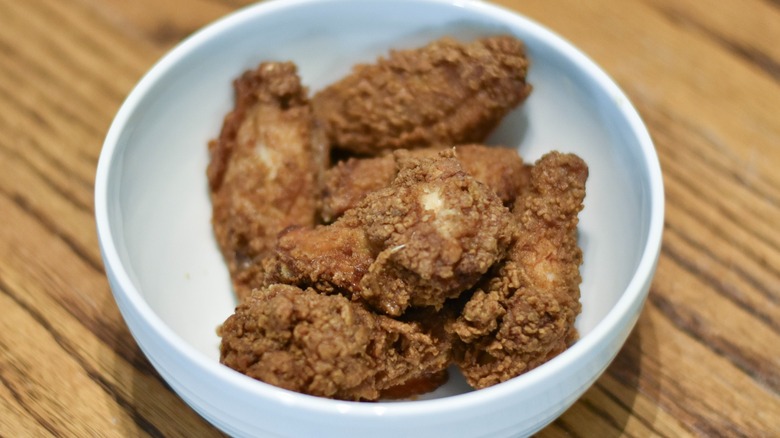 A white bowl of bone-in chicken wings on a wooden table