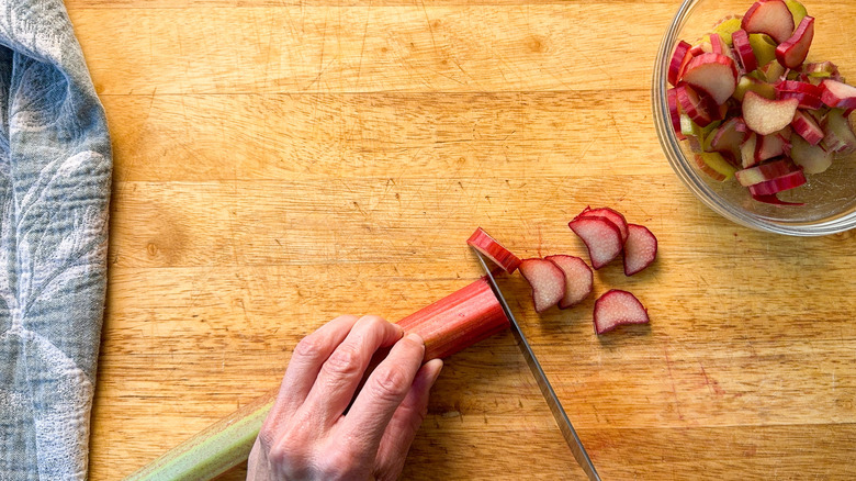 Slicing rhubarb stalks on cutting board with bowl of rhubarb