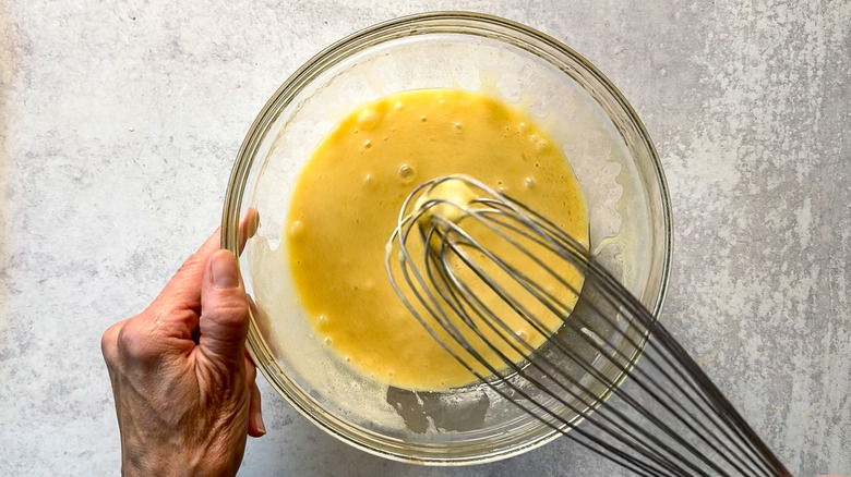 Whisking together eggs, oil, milk and vanilla in glass bowl on countertop