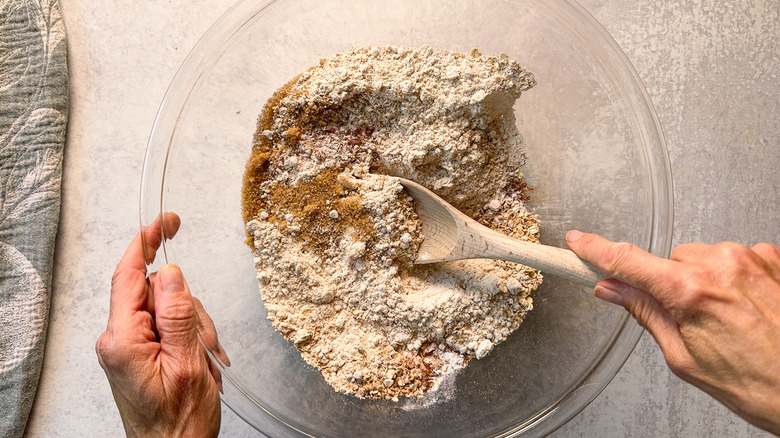 Mixing together dry ingredients for rhubarb and cardamom oat muffins in glass bowl with wooden spoon