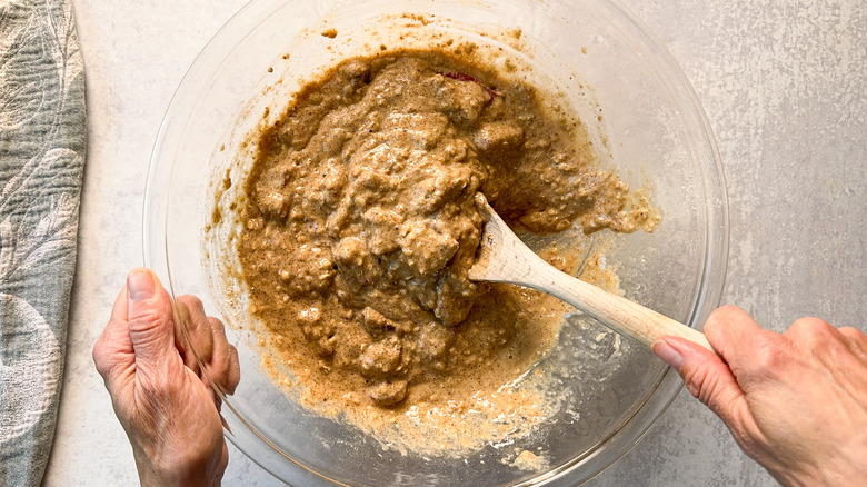 Stirring rhubarb and cardamom oat muffin batter in glass bowl with wooden spoon