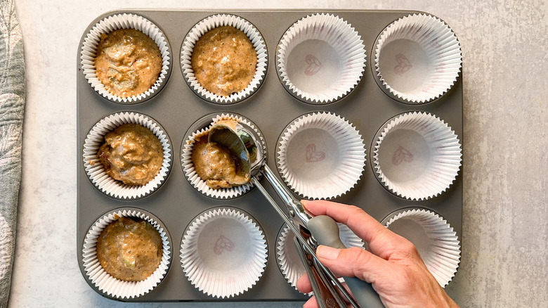 Scooping rhubarb and cardamom oat muffin batter into muffin papers in muffin tin