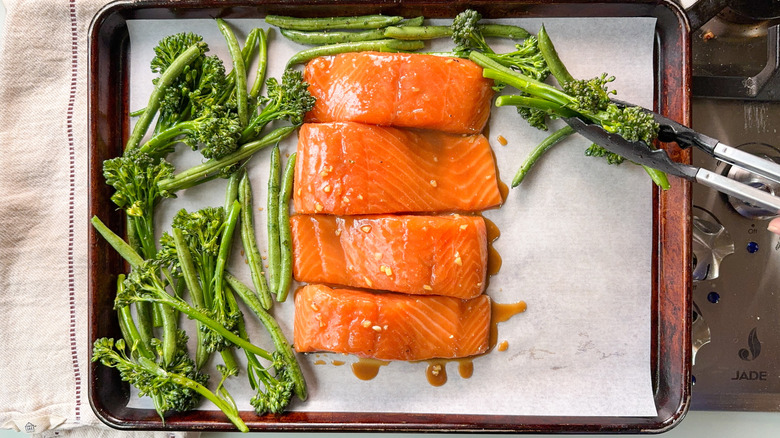 Miso maple marinated salmon fillets on parchment lined baking sheet with broccolini and green beans