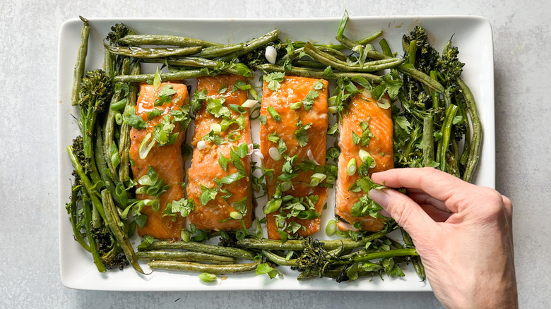 Garnishing roasted miso maple salmon with scallions and cilantro on serving platter with broccolini and green beans