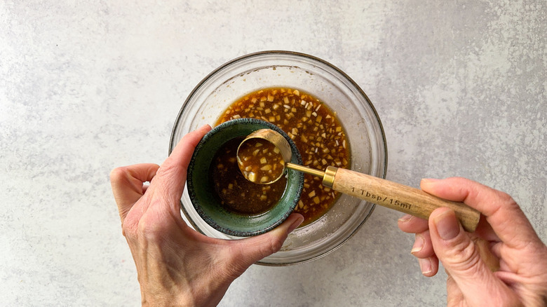 Measuring out 2 tablespoons of miso maple marinade from glass bowl with measuring spoon