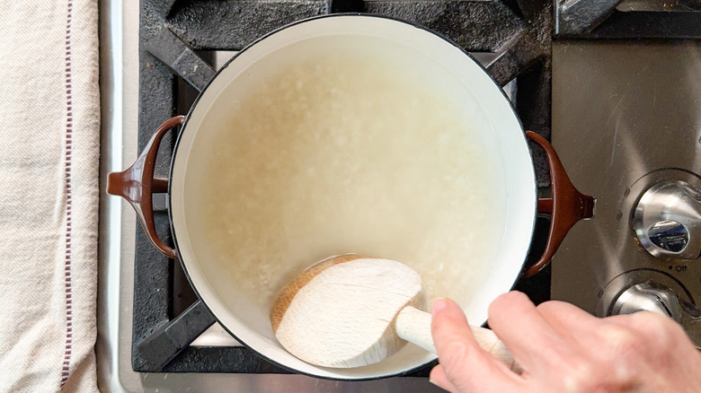 Stirring white rice in water in pot on stovetop