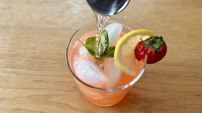 clear liquid from shot glass being poured into pink lemonade