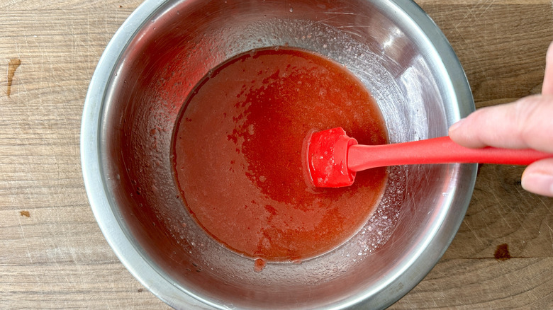 hand stirring pureed strawberries in metal bowl