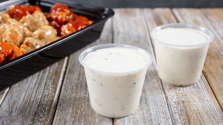 Two cups of ranch sitting on a wooden surface