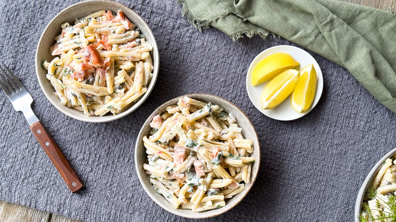 Salmon dill pasta salad in bowls on table with lemon wedges