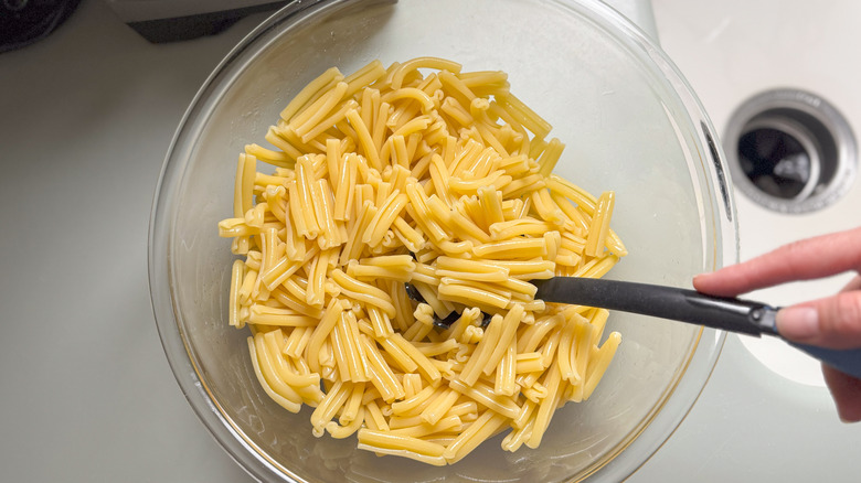 Tossing cooked pasta with olive oil in glass bowl