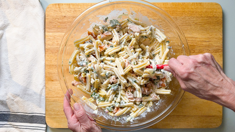 Mixing salmon dill pasta salad in glass bowl with spatula