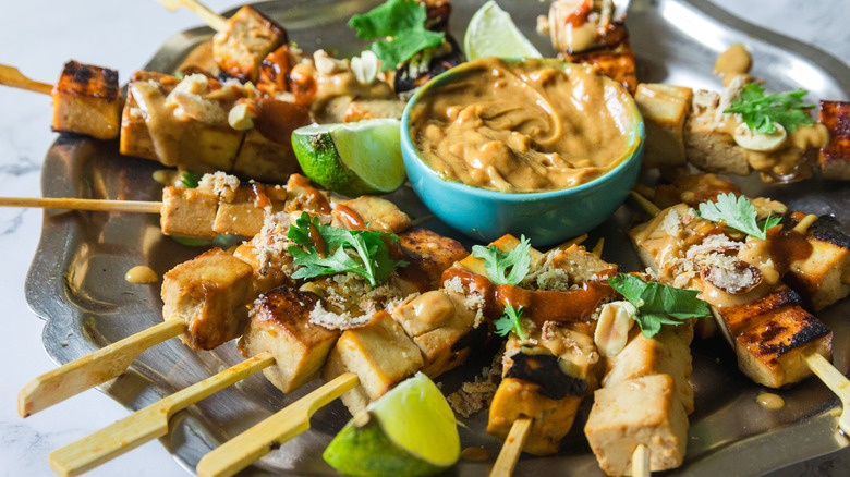 Close up on satay tofu skewers with peanut sauce on a metal plate