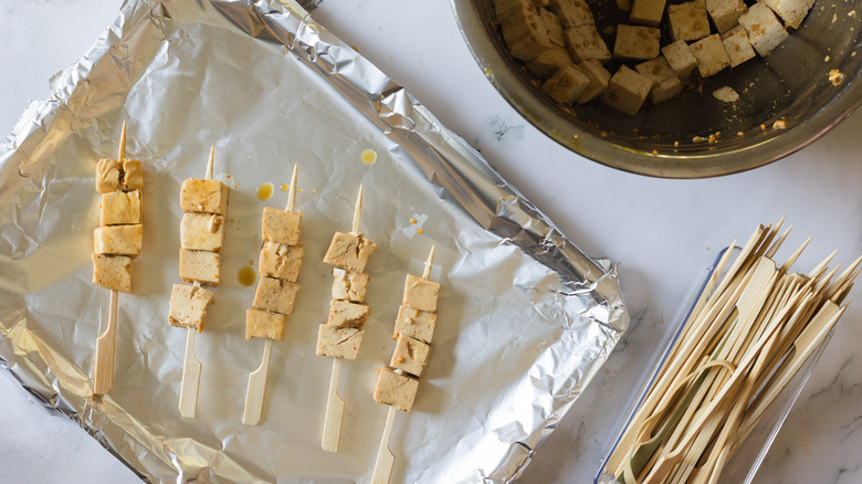 tofu on skewers on aluminum covered sheet alongside skewers