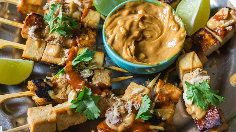 Close up on satay tofu skewers with peanut sauce on a metal plate