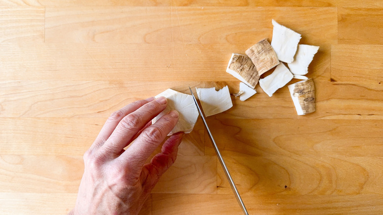 Removing peel from horseradish root with knife on cutting board