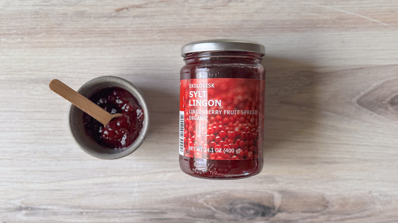 Jar and bowl of lingonberry preserves with wooden spoon