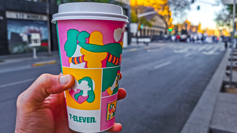 A person holding a to-go cup of 7-Eleven cup of coffee