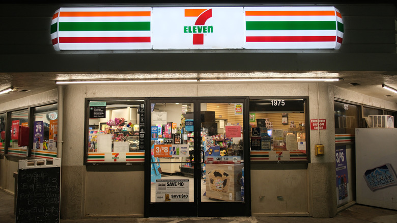 The exterior of a 7-Eleven store at night with the sign illuminated