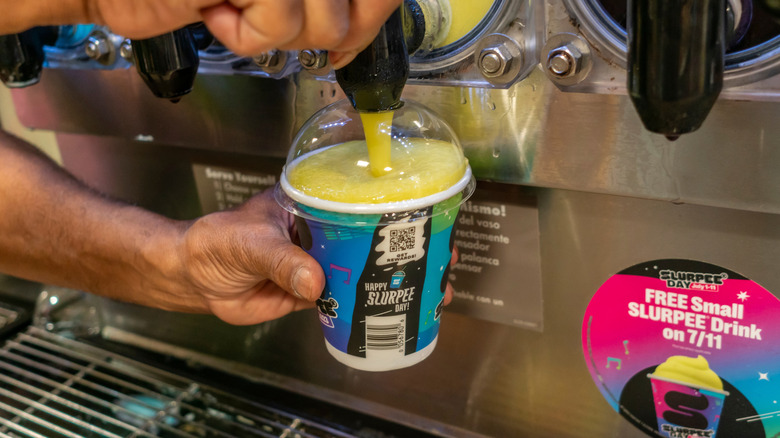 A person fills a small slurpee cup on free slurpee day with yellow icy drink