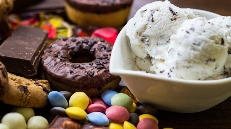 A doughnut and assorted candies and toppings beside a bowl of ice cream