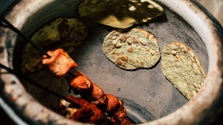 Naan bread and meat skewers inside a tandoor