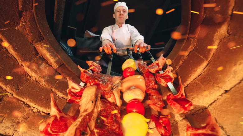 Chef cooking meat and vegetables inside a tandoor