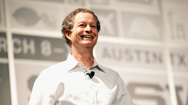 Whole Foods CEO John Mackey speaking on stage wearing a white button-down shirt