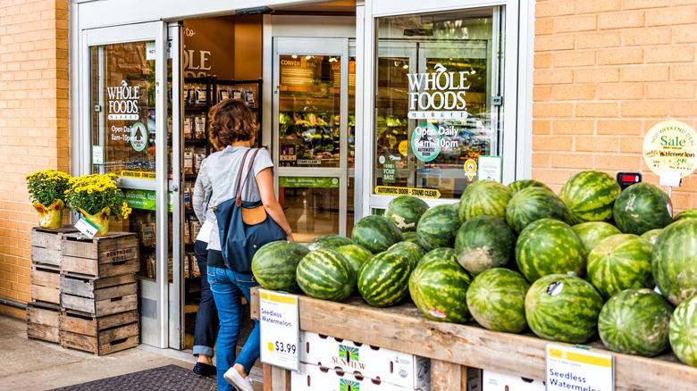 A woman walks into Whole Foods Market with a display of watermelons and yellow flowers outside