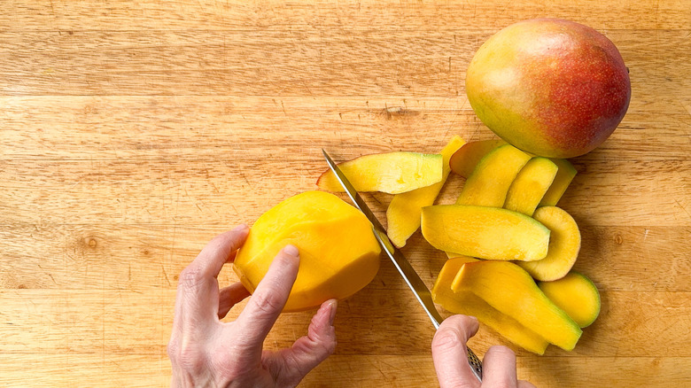 Cutting the peel away from mangoes on a cutting board