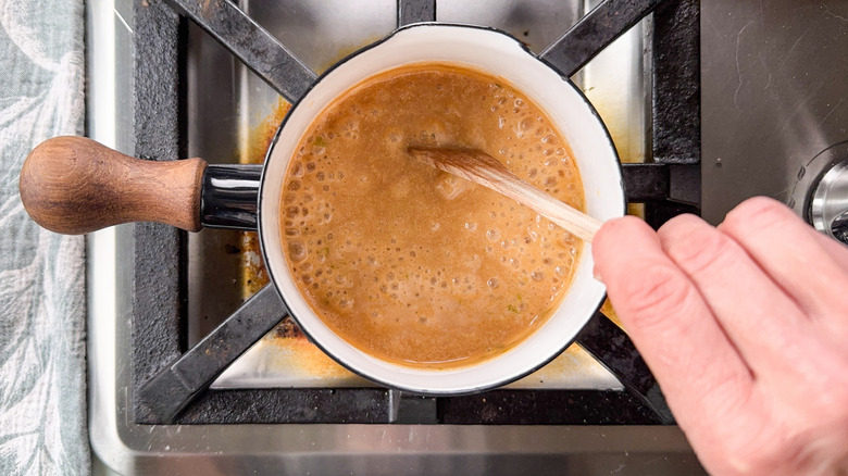 Stirring coconut milk and coconut sugar cooking in pot on stovetop